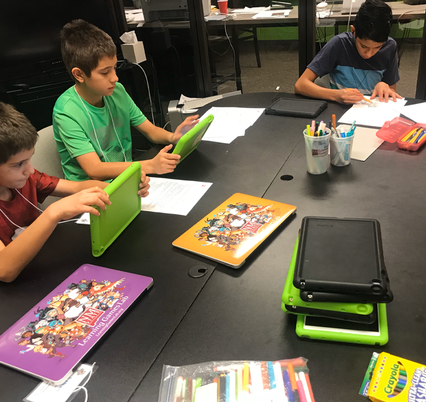 Students at a table using a tablet and writing