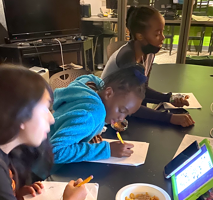 Three students at a table taking notes